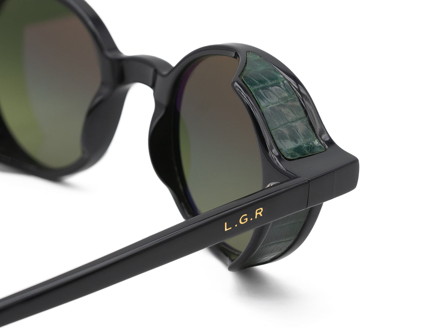 Close-up of black L.G.R. Reunion sunglasses with green crocodile textured side shields and gold logo