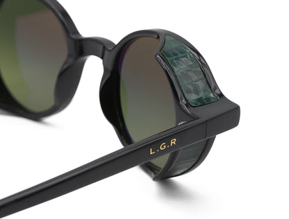 Close-up of black L.G.R. Reunion sunglasses with green crocodile textured side shields and gold logo