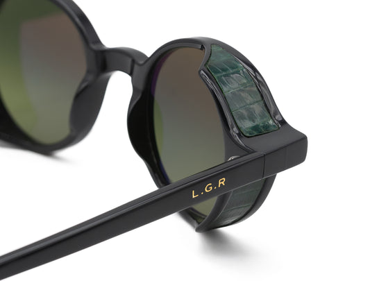 Close-up of black L.G.R. Reunion sunglasses with green crocodile textured side shields and gold logo