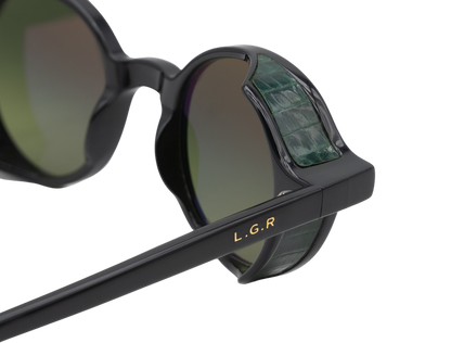 Close-up of black L.G.R. Reunion sunglasses with green crocodile textured side shields and gold logo